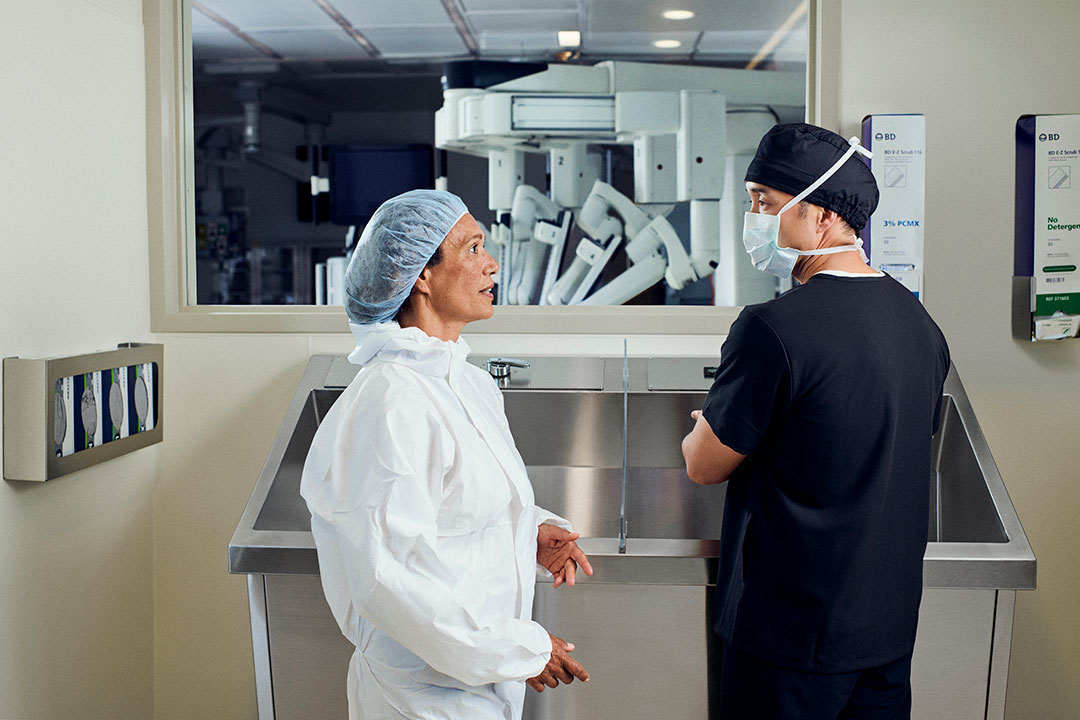 Two healthcare workers scrubbing in for surgery with da Vinci system in background